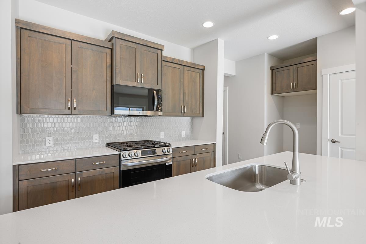 205 West Broyhill Street Meridian, ID 83642 - Photo 3 of 20 Kitchen featuring stainless steel appliances, light stone countertops, backsplash, recessed lighting, and dark wood finish cabinetry