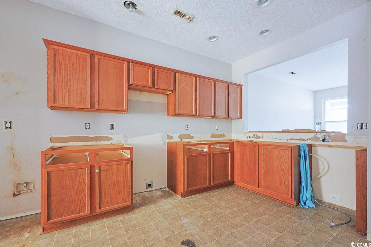 308 Kiskadee Loop, Unit E Conway, SC 29526 - Photo 8 of 28 Kitchen with brown cabinetry, a textured ceiling, a peninsula, and light countertops