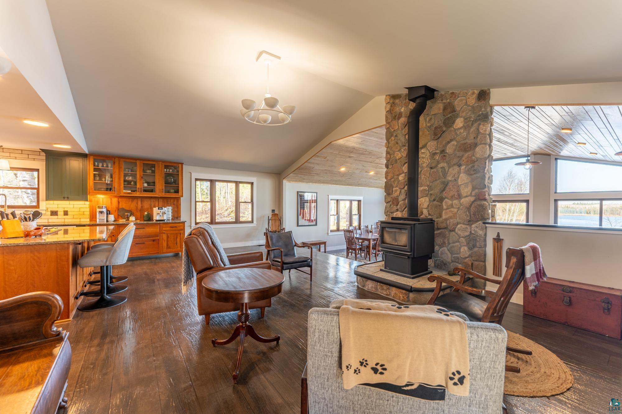 14635 Canadian Border Road Ely, MN 55731 - Photo 49 of 94 Stone-faced fireplace with a wood-burning stove, rich wood-finish flooring, vaulted wood-paneled ceiling, and expansive windows