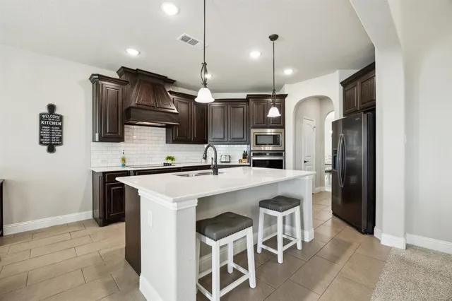a kitchen with kitchen island stainless steel appliances a sink a stove a microwave a refrigerator and cabinets