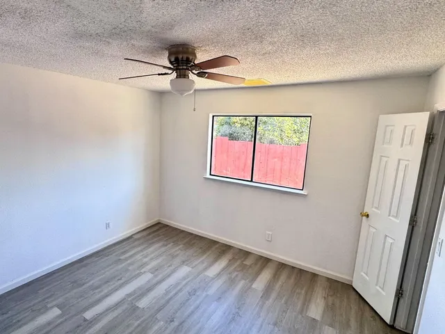 an empty room with wooden floor fan and windows