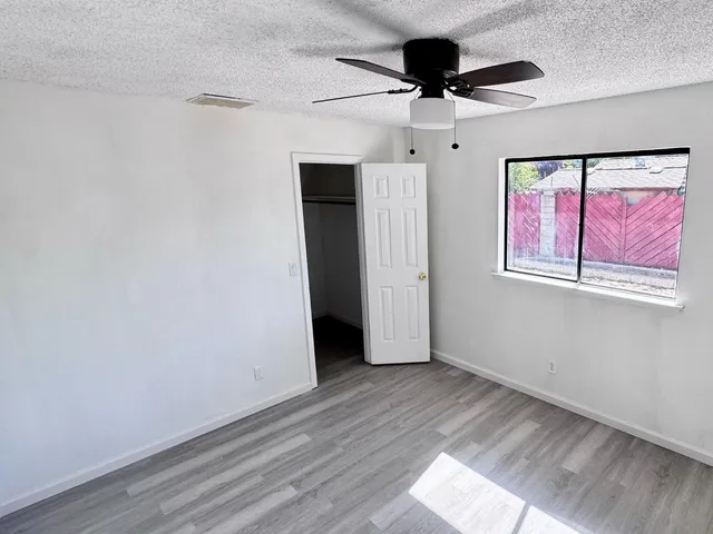 an empty room with wooden floor chandelier fan and windows
