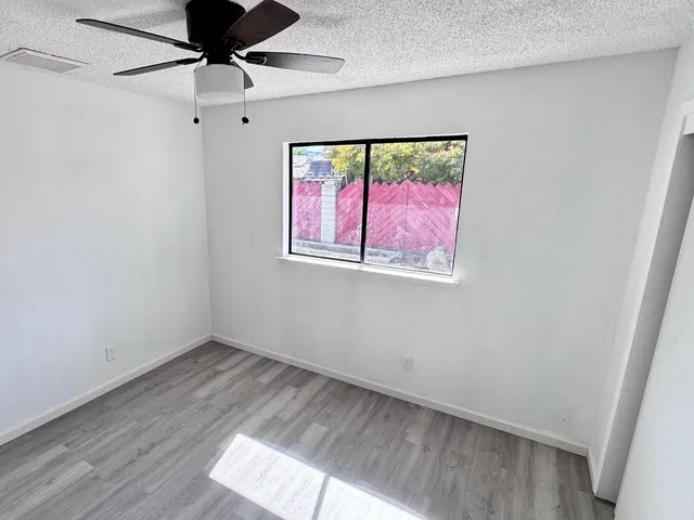 an empty room with wooden floor fan and windows