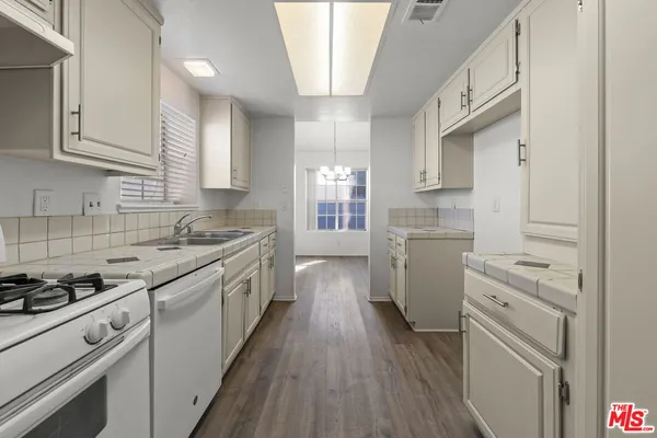 a kitchen with granite countertop white cabinets a sink dishwasher and a stove with wooden floor