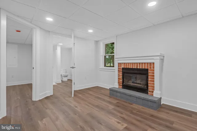 a view of an empty room with wooden floor fireplace and a window