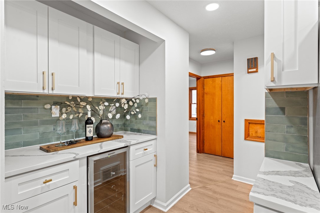5266 Wilson Mills Road Cleveland, OH 44143 - Photo 21 of 50 Indoor bar with white cabinetry, beverage cooler, light stone countertops, decorative backsplash, and light wood-type flooring