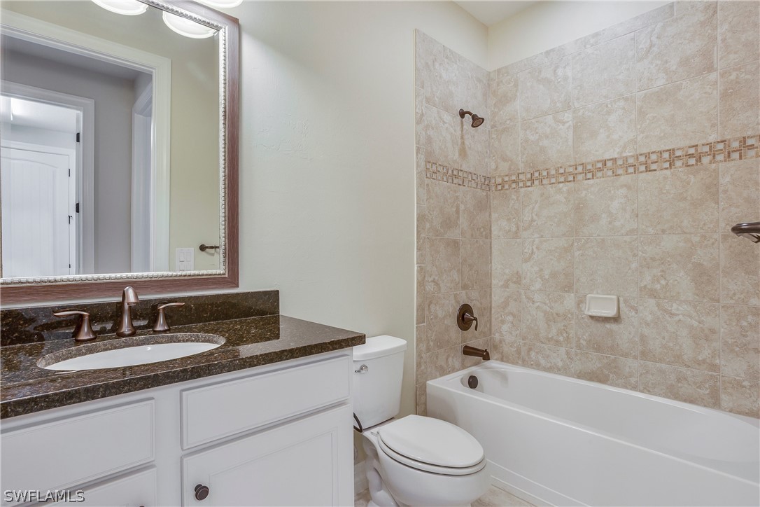 10828 Rutherford Road Fort Myers, FL 33913 - Photo 19 of 31 a bathroom with a granite countertop sink a toilet a mirror a bathtub and shower