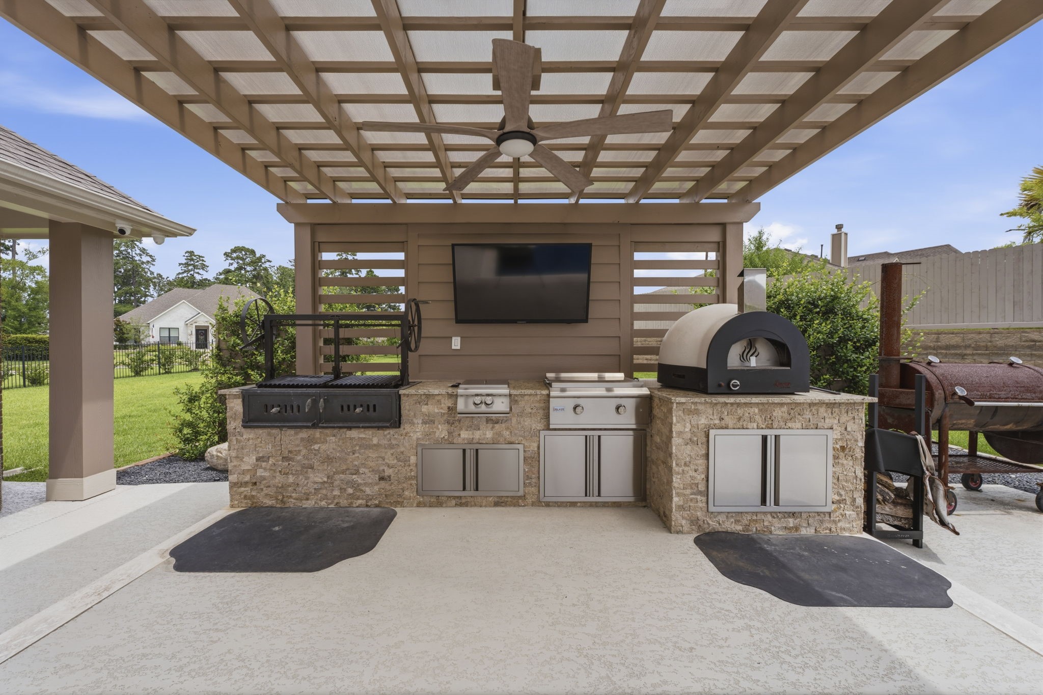 14012 Beartooth Bend Trail Conroe, TX 77384 - Photo 37 of 50 Equipped with a premium built-in Sunterra live-fire “Santa Maria” grill with adjustable grate, flat top grill with side burner, and Italian imported pizza oven, this space combines luxury with functionality. Complete with a lighted ceiling fan for comfort, this outdoor culinary retreat is perfectly suited for everything from casual weekends to elegant outdoor celebrations. Please exclude TV.