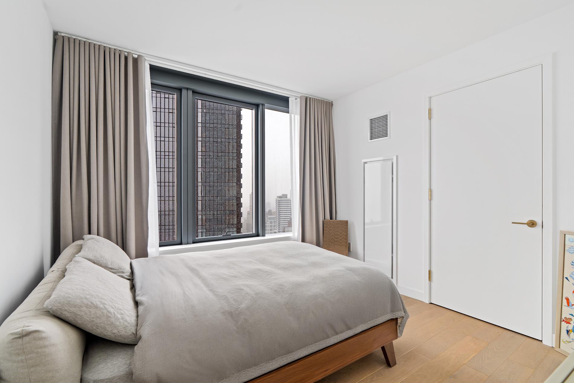 3 Court Square, Unit 2902 Queens, NY 11101 - Photo 3 of 12 a bed sitting in a bedroom next to a window