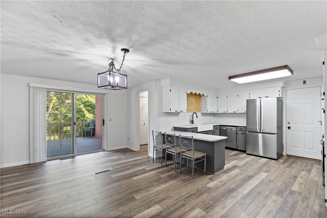 Kitchen with stainless steel appliances, a peninsula, gray cabinetry, decorative light fixtures, and white cabinets