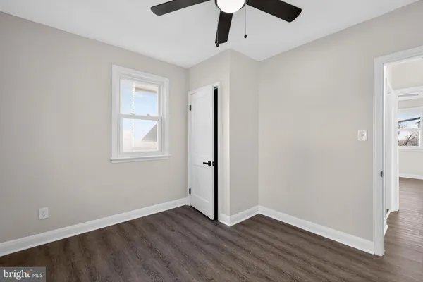 a view of an empty room with wooden floor and a ceiling fan