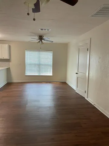 an empty room with wooden floor chandelier fan and windows