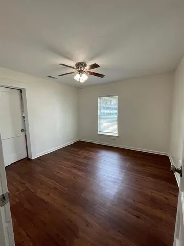 an empty room with wooden floor fan and windows