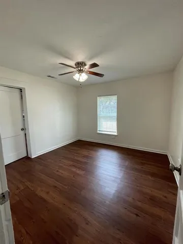 an empty room with wooden floor fan and windows