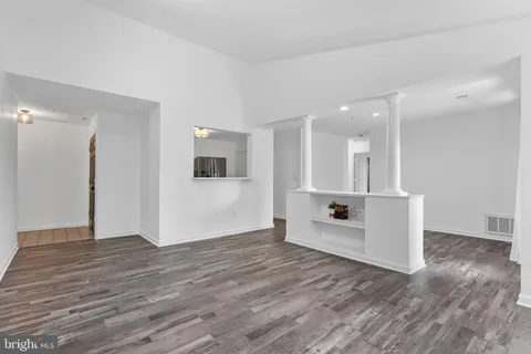 a view of an empty room with wooden floor and a kitchen
