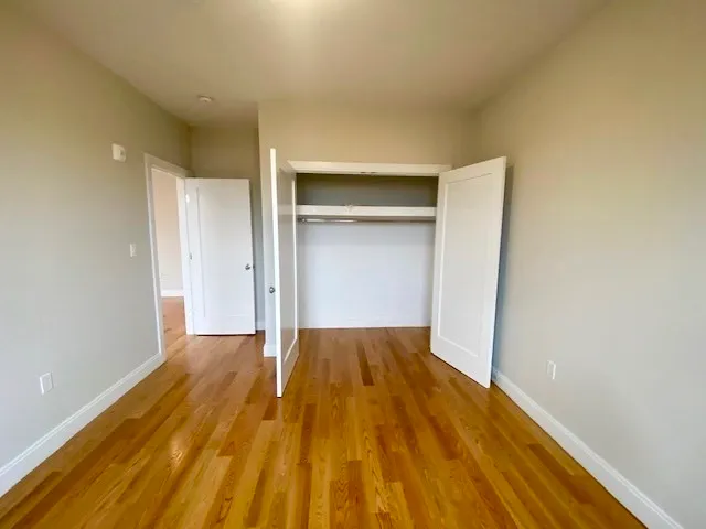 a view of an empty room with wooden floor and closet