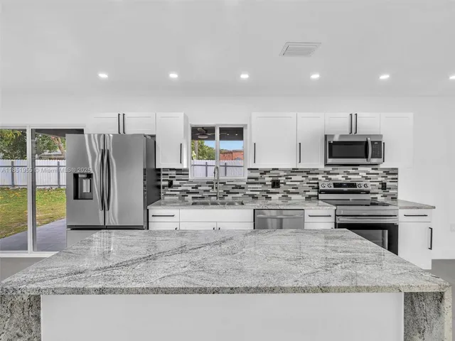 a large white kitchen with refrigerator a sink and a large window