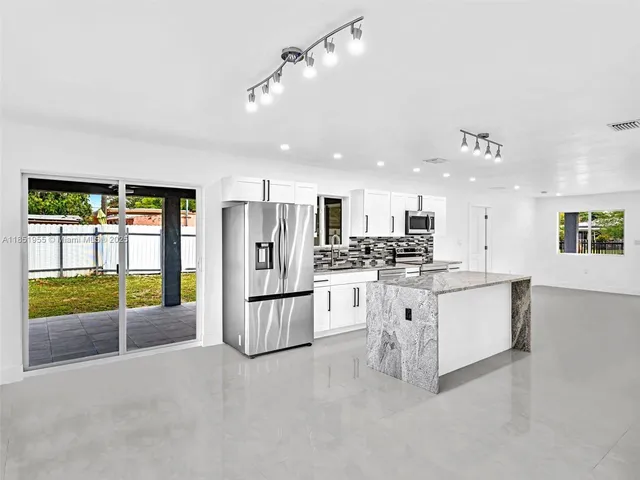 a large kitchen with stainless steel appliances kitchen island granite countertop a refrigerator and a sink