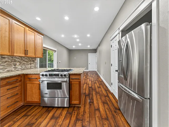 a kitchen with stainless steel appliances granite countertop a refrigerator a stove and a wooden floors