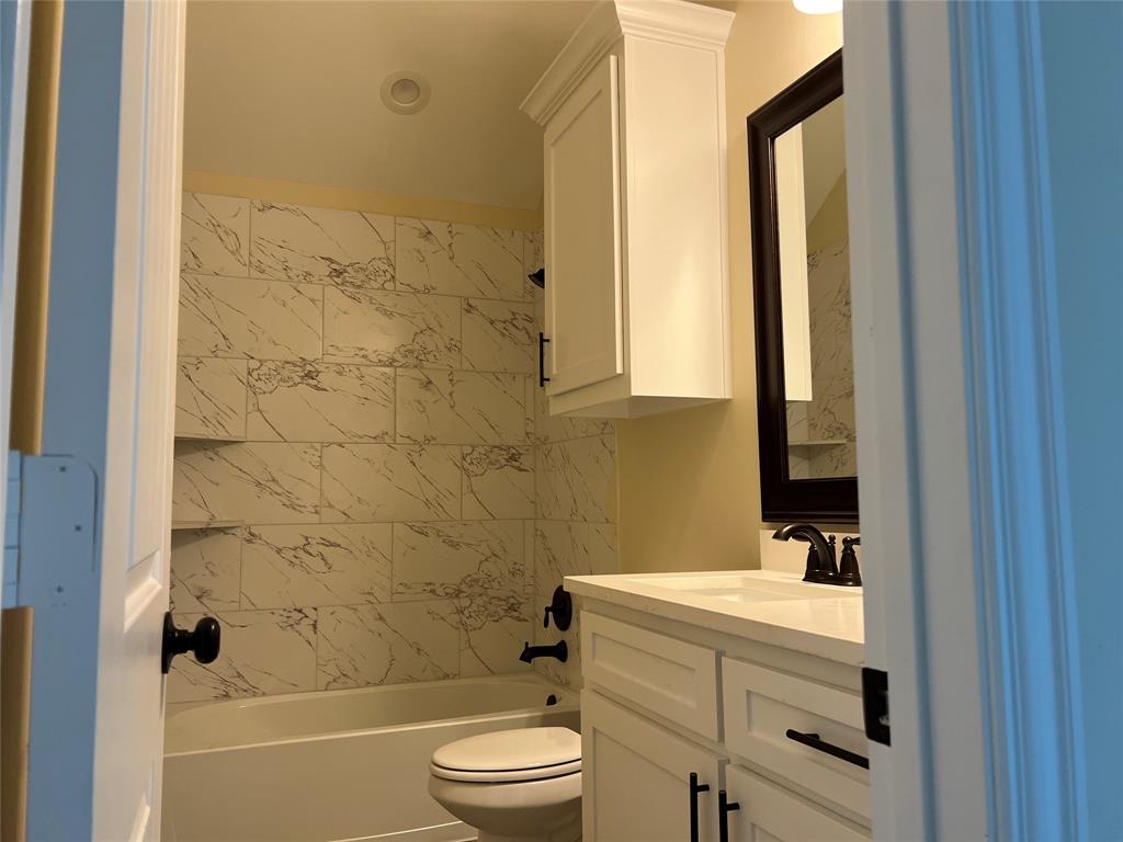 8008 County Road 1058 Rice, TX 75155 - Photo 21 of 25 Bathroom featuring a white bathtub with marble-style tile surround, white vanity with integrated sink, white upper cabinet, and dark-framed mirror