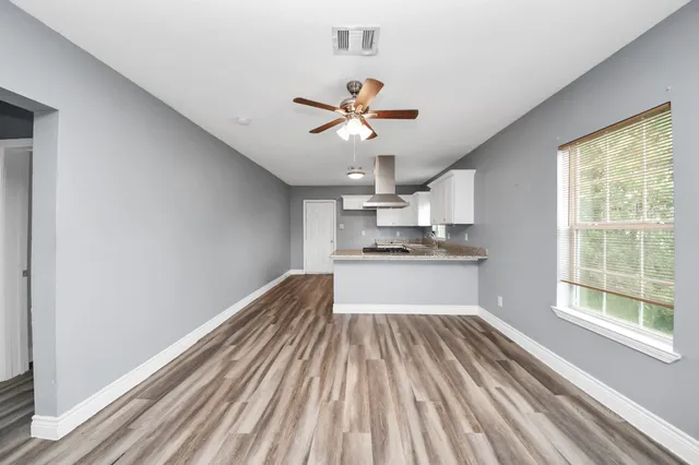 a view of a kitchen with wooden floor a ceiling fan and windows