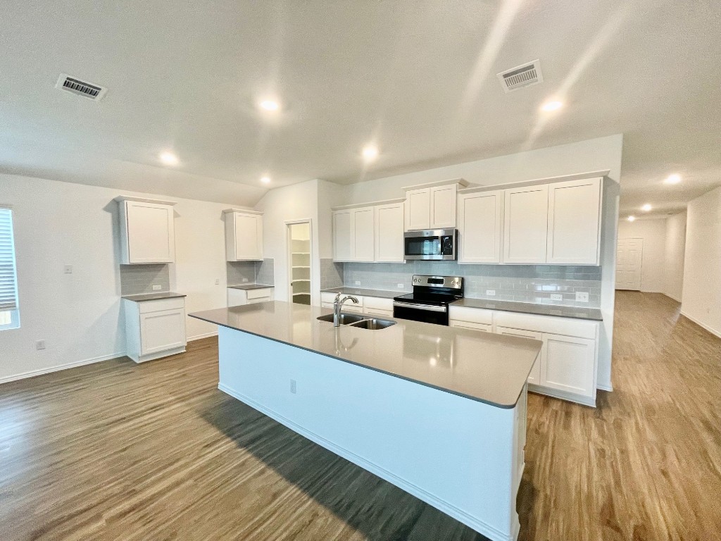 a large white kitchen with wooden floors stainless steel appliances and cabinets