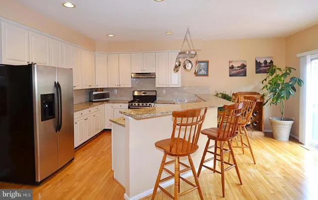 a kitchen with stainless steel appliances kitchen island granite countertop a refrigerator a stove a sink dishwasher and white cabinets with wooden floor