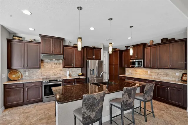 a kitchen with stainless steel appliances granite countertop a stove top oven a refrigerator a sink and chairs