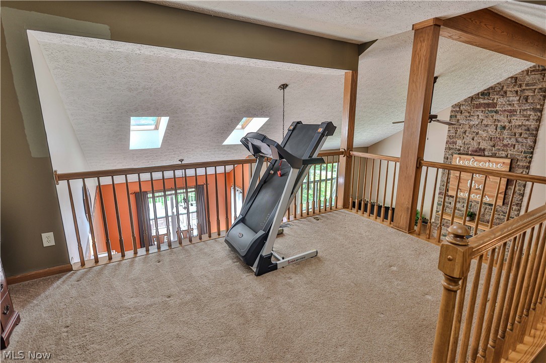 11154 Johnsford Road Southwest Beach City, OH 44608 - Photo 43 of 50 Carpeted loft space featuring wood railings, exposed wood beams, and a vaulted ceiling with skylights, overlooking a lower level with brick accent wall and ceiling fan