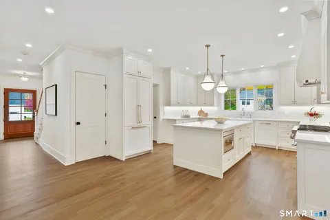 a large white kitchen with kitchen island a chandelier stainless steel appliances cabinets and wooden floor