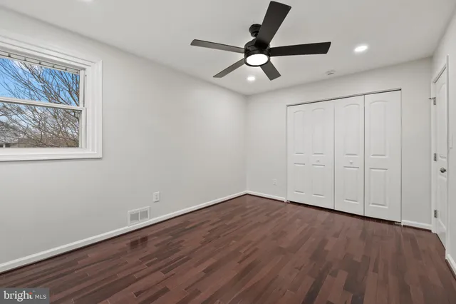 a view of an empty room with wooden floor and a ceiling fan