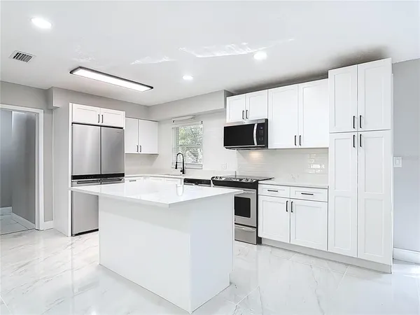 a kitchen with stainless steel appliances granite countertop a stove top oven a sink a refrigerator and white cabinets with wooden floor