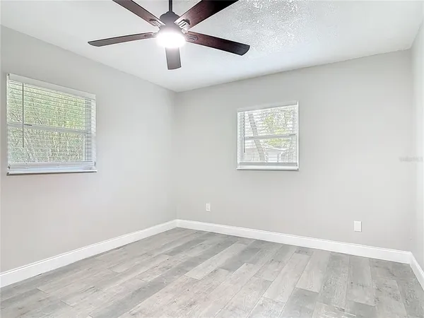 an empty room with wooden floor ceiling fan and windows