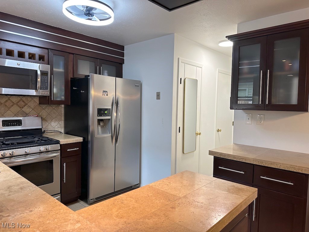 6482 State Road, Unit E1 Parma, OH 44134 - Photo 17 of 48 Kitchen with appliances with stainless steel finishes, decorative backsplash, glass insert cabinets, and dark brown cabinets