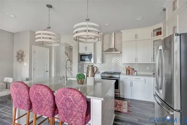 a kitchen with stainless steel appliances granite countertop a refrigerator a sink dishwasher a stove a dining table and chairs with wooden floor