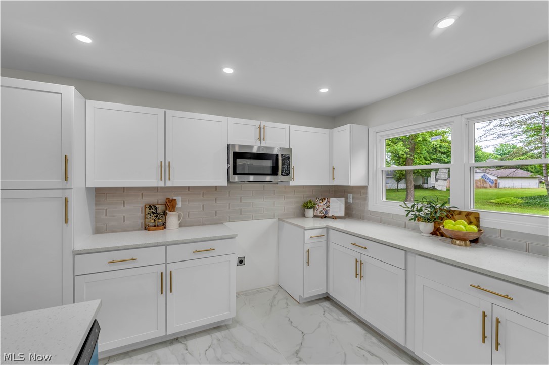 10763 Gate Post Road Strongsville, OH 44149 - Photo 14 of 45 Kitchen featuring white shaker cabinetry with gold-tone hardware, a stainless steel microwave, light-toned quartz countertops, and a subway tile backsplash