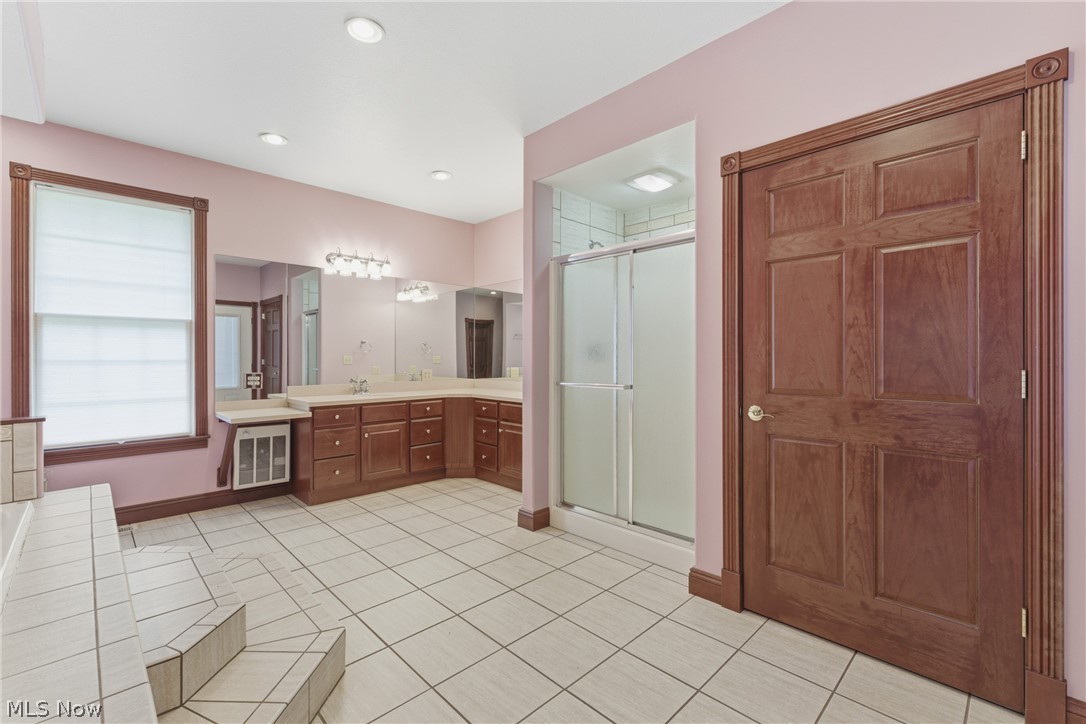 2184 Brenner Road Northeast Carrollton, OH 44615 - Photo 20 of 50 Spacious bathroom featuring light-colored tile flooring, a double vanity with built-in cabinetry, a window with a white privacy shade, an enclosed shower, and a paneled door with decorative trim