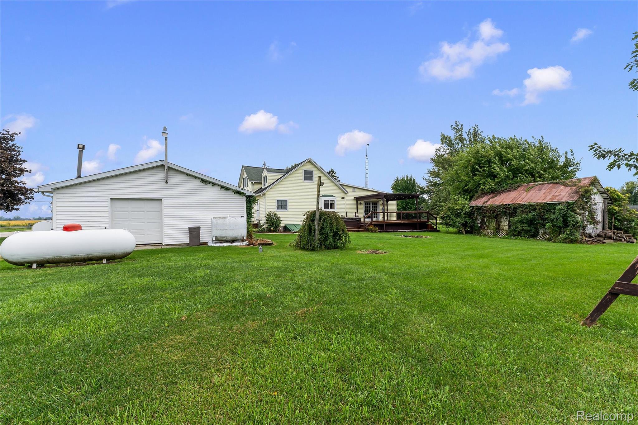 3553 North State Road Owosso, MI 48867 - Photo 33 of 45 Expansive green lawn featuring a white outbuilding with a roll-up door, a detached wood deck, and an additional shed with a metal roof