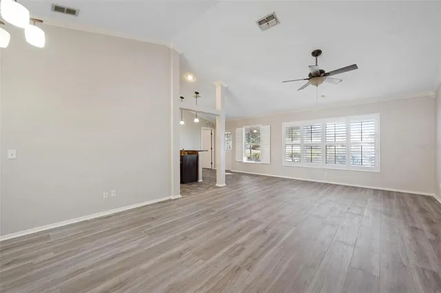 an empty room with wooden floor ceiling fan and windows