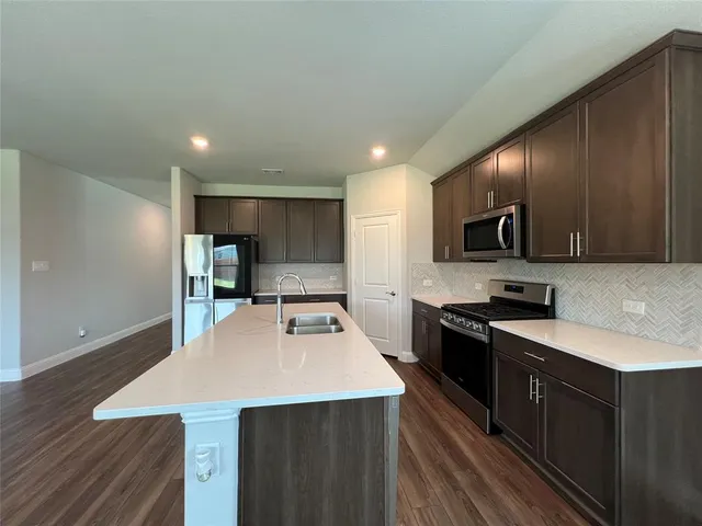 a kitchen with stainless steel appliances kitchen island granite countertop a sink a stove top oven a counter space and cabinets