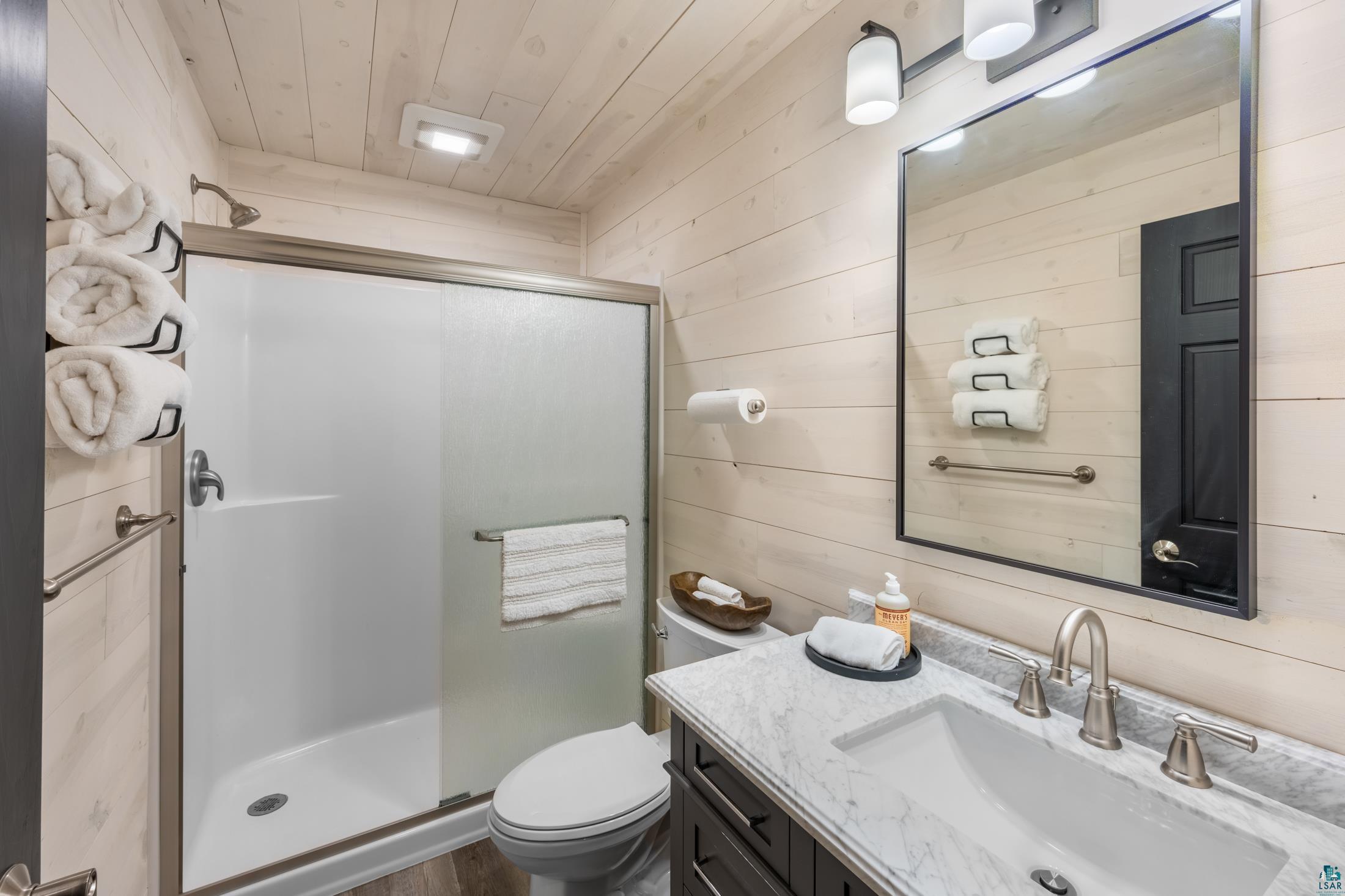 3778 East County Road Barnum, MN 55707 - Photo 24 of 52 Integrated shower with sliding glass doors, single vanity with a stone countertop, wall-mounted mirror, and wood-finish wall paneling
