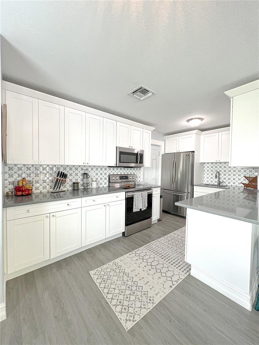 515 Valley Forge Road West Palm Beach, FL 33405 - Photo 3 of 9 a kitchen with stainless steel appliances kitchen island granite countertop a stove a sink and white cabinets
