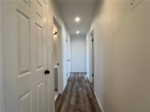 a view of a hallway with wooden floor and a bathroom