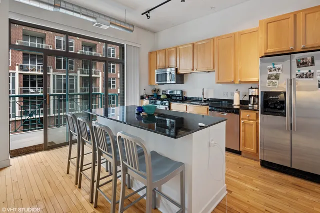 a kitchen with stainless steel appliances granite countertop a stove a refrigerator a sink a dining table and chairs with wooden floor