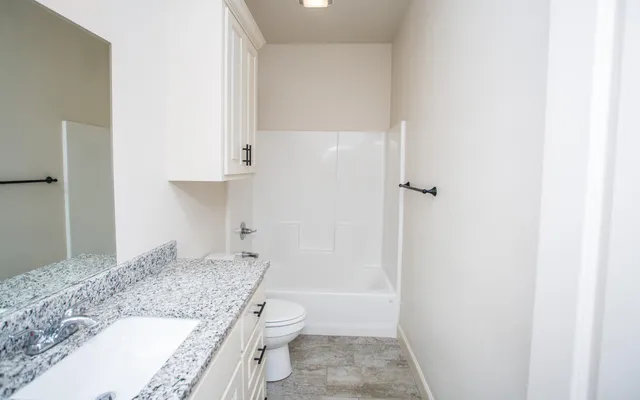a bathroom with a granite countertop sink a toilet and shower