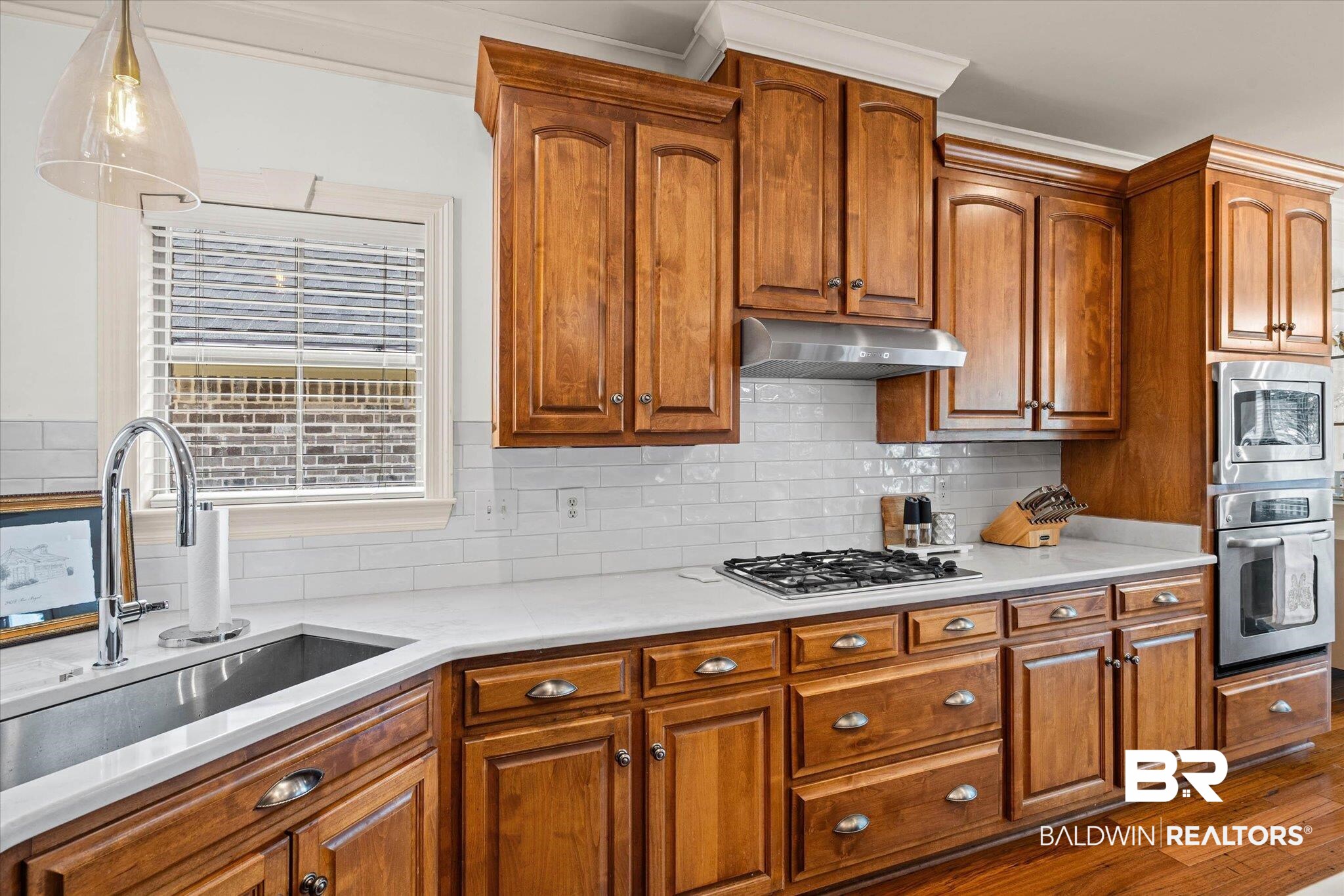 3459 Rue Royal Mobile, AL 36693 - Photo 10 of 31 Kitchen featuring rich wood cabinetry with crown molding, light-toned countertops, a stainless steel undermount sink, a gas cooktop with a range hood, and integrated double ovens