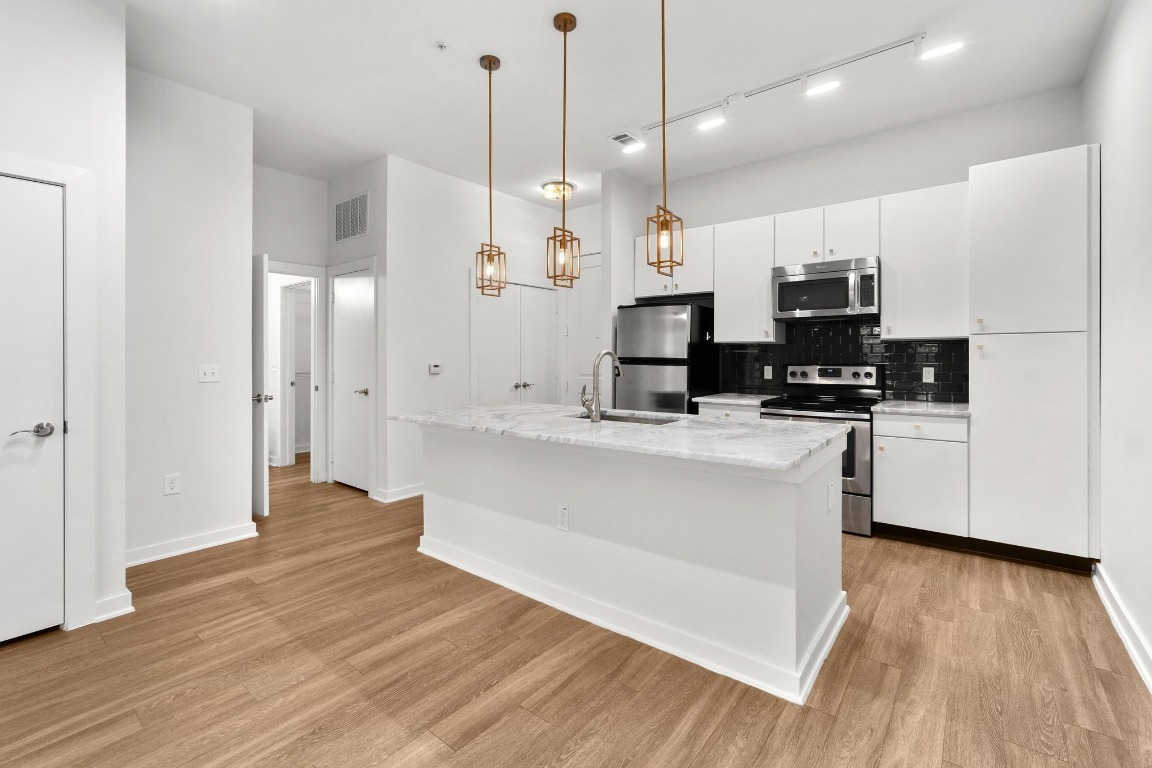 1900 Barton Springs Road, Unit 2035 Austin, TX 78704 - Photo 1 of 1 a kitchen with stainless steel appliances kitchen island granite countertop a stove a refrigerator a sink and a microwave with wooden floor