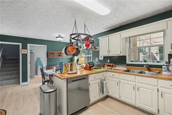 a kitchen with a sink dishwasher a stove and white cabinets with wooden floor
