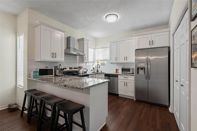 a kitchen with stainless steel appliances granite countertop a stove a sink dishwasher a refrigerator with white cabinets and wooden floor