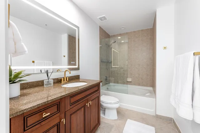 a bathroom with a granite countertop bathtub shower sink vanity mirror and toilet